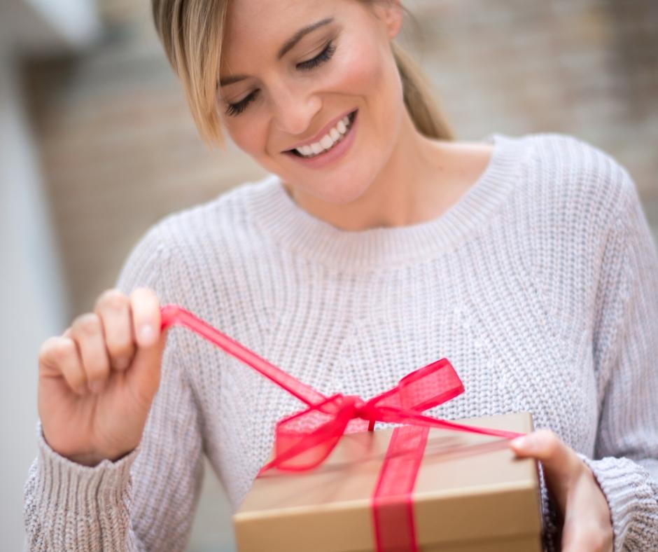 Woman with glowing skin smiling and unwrapping a holiday gift of a skin treatment gift certificate from an aesthetics clinic